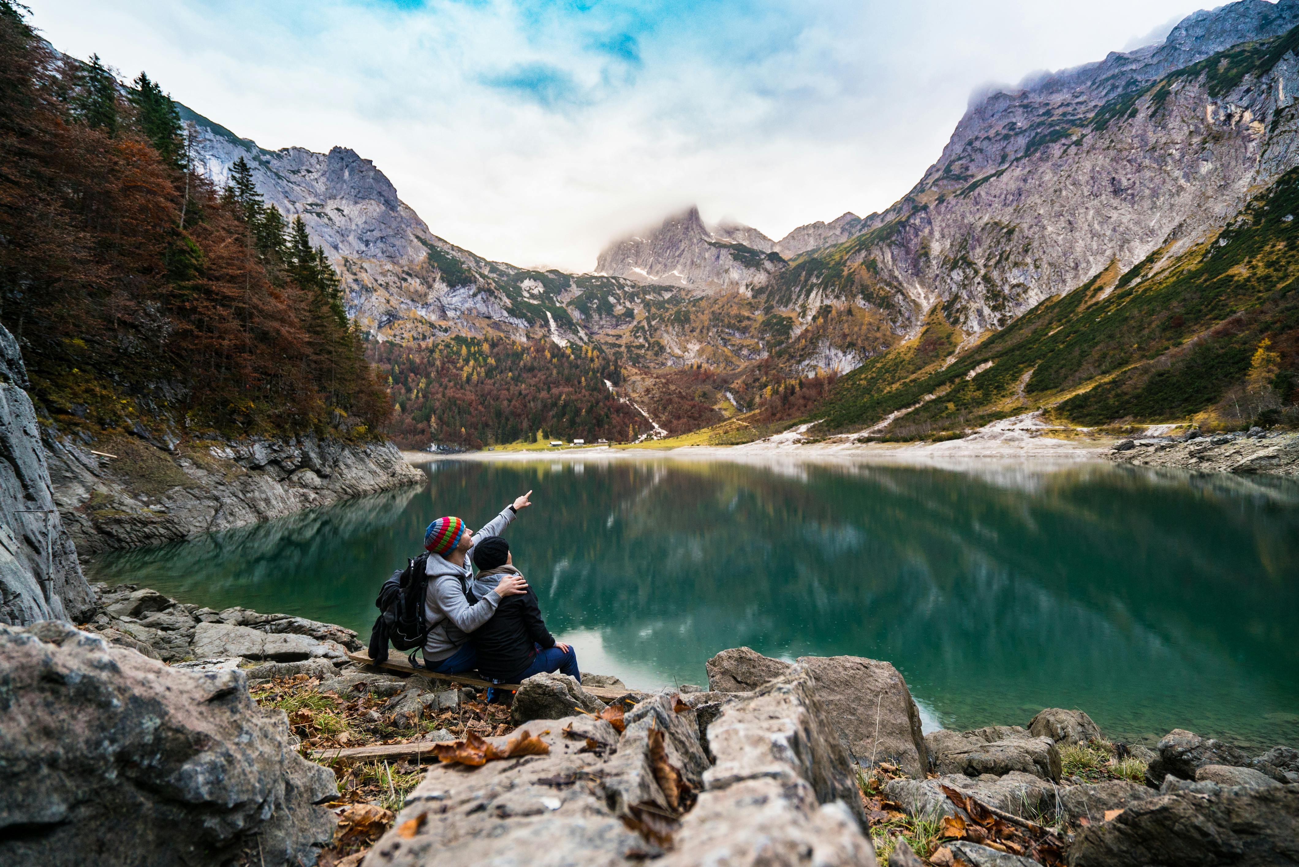 Ein Paar sitzt am Rand eines Bergsees und blickt auf die umgebende Berglandschaft.
